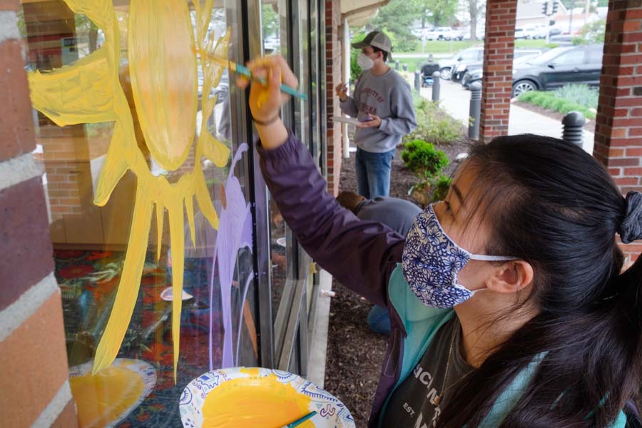 A woman in a mask paints a yellow sun on the window of a building