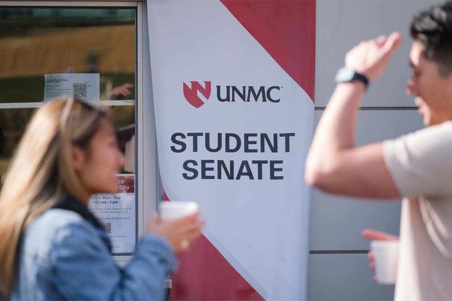 Two students stand in front of a banner that says "UNMC Student Senate"