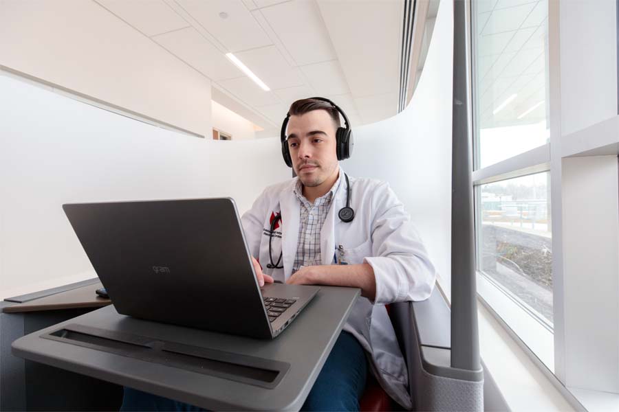 A man in a white coat wearing headphones looks at a laptop
