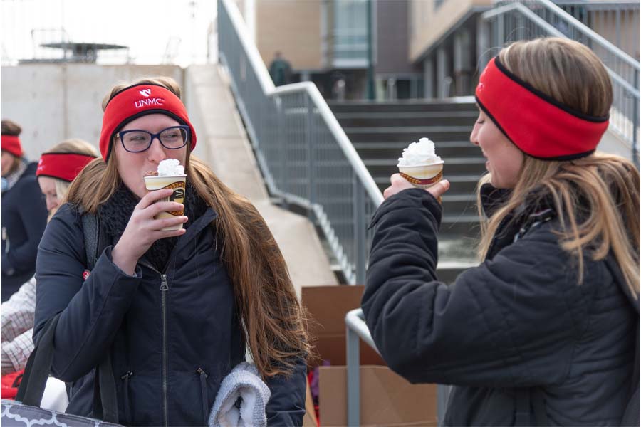 Two women drink hot chocolate outside the UNMC Ice Rink
