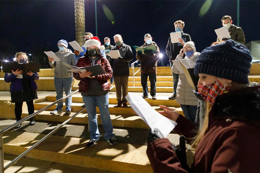 A group of people in masks hold music sheets during a caroling event
